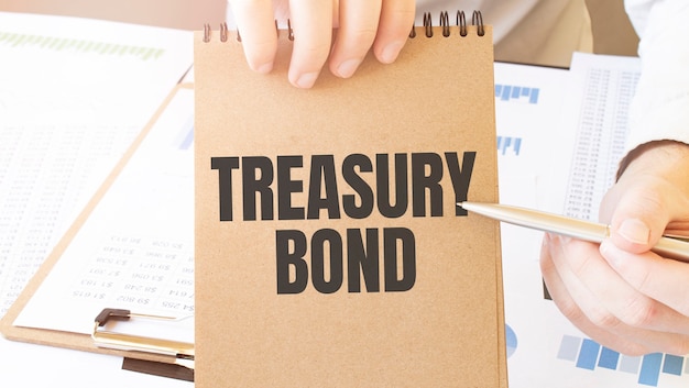 Text treasury bond on brown paper notepad in businessman hands on the table with diagram.