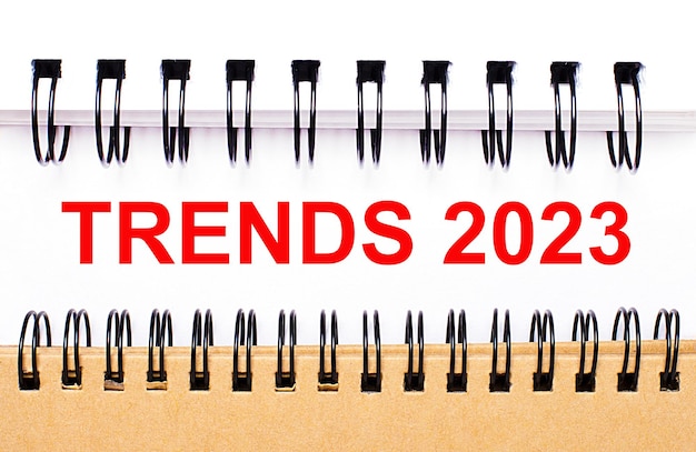 Текст trends 2023 на белой бумаге между белыми и коричневыми спиральными блокнотами