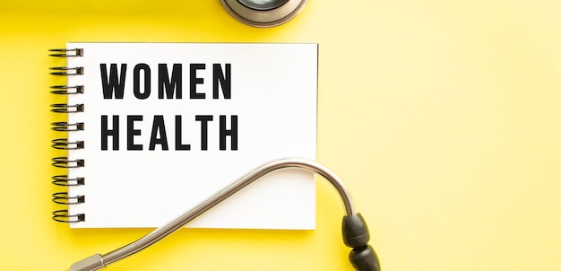 Text women health on notebook with stethoscope on yellow background