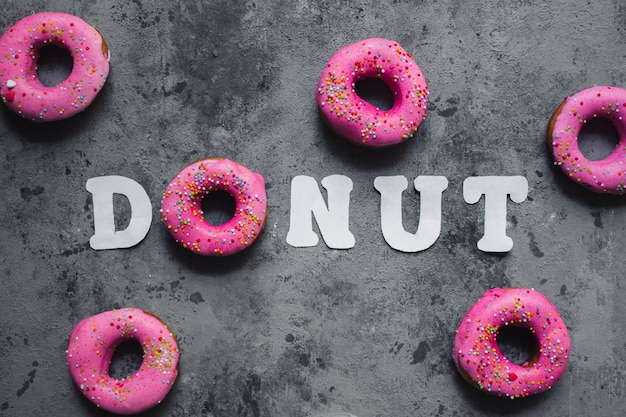 Photo text word donut made of one pink rainbow sprinkles doughnut and white paper letters on grey dark