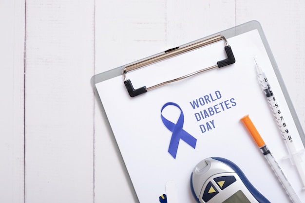 Text World Diabetes Day and blue ribbon on tablet with glucometer and syringes