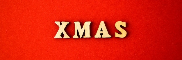 Text XMAS made of wooden letters on red background. Banner size. New year and Merry Christmas greeting card. Wood letter