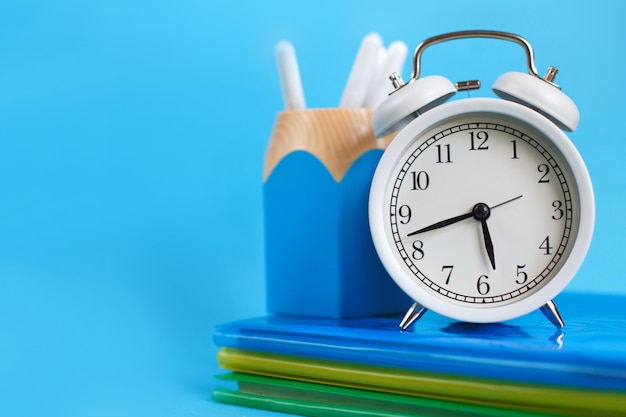 Textbooks and alarm clock on a blue background