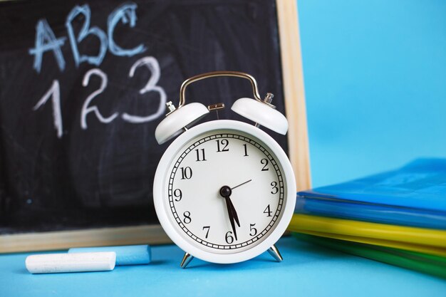 Textbooks and alarm clock with school chalkboard on a blue background