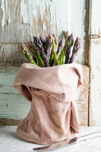 Foto borsa del tessuto con il mazzo di asparagi organici naturali freschi contro la vecchia parete di legno.