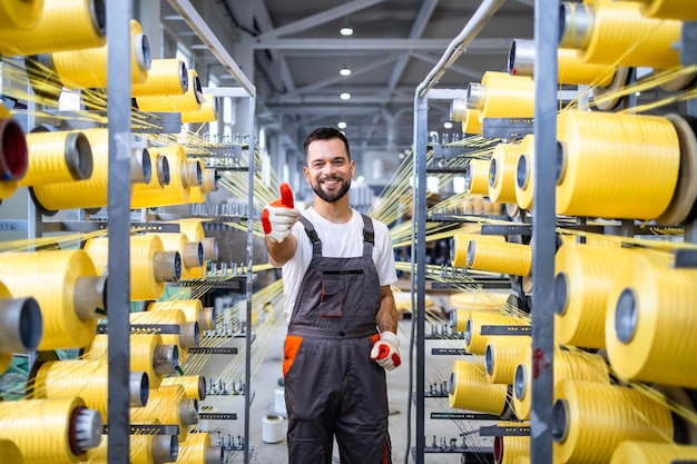 Textile factory worker holding thumbs up by industrial knitting machine