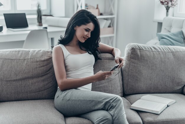 Texting to boyfriend. Beautiful young woman using smart phone while relaxing on couch at home