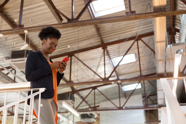 Texting her client. Dark-skinned designer wearing orange blouse texting her client while having questions