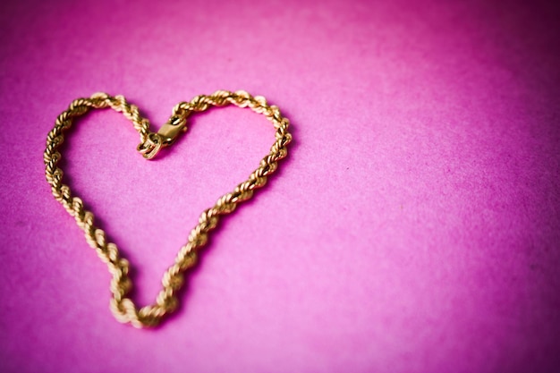 Texture of a beautiful golden festive chain unique weaving in the shape of a heart on a pink purple