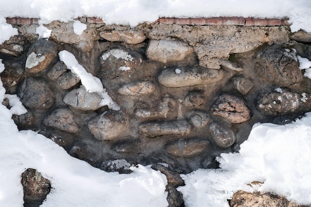 Texture di pietre di ciottoli nel vecchio muro di cemento in inverno con la neve