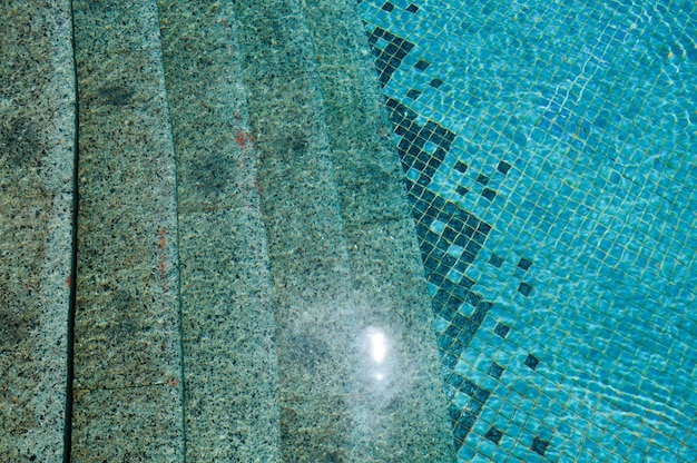 The texture of the entrance of the descent into the pool with blue water and square ceramic tiles