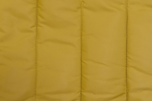 Texture of the fabric for a winter down jacket of ocher color closeup