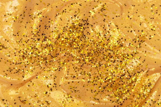 Texture of a flowing gold cosmetic product or acrylic paint covered in glitter
