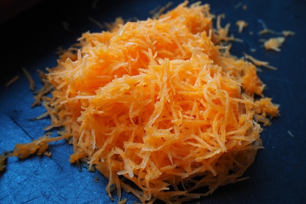 Texture of grated carrot Daucus carota subsp sativus Root vegetable orange in color Grated carrots on a black cutting board