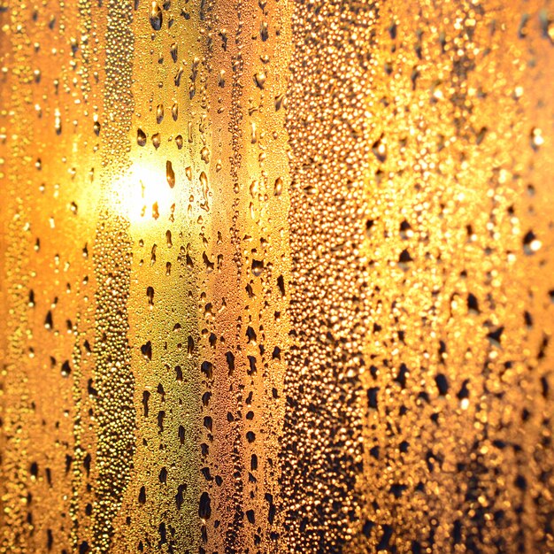 The texture of misted glass with a lot of drops and drips of condensation against the sunlight at dawn. 