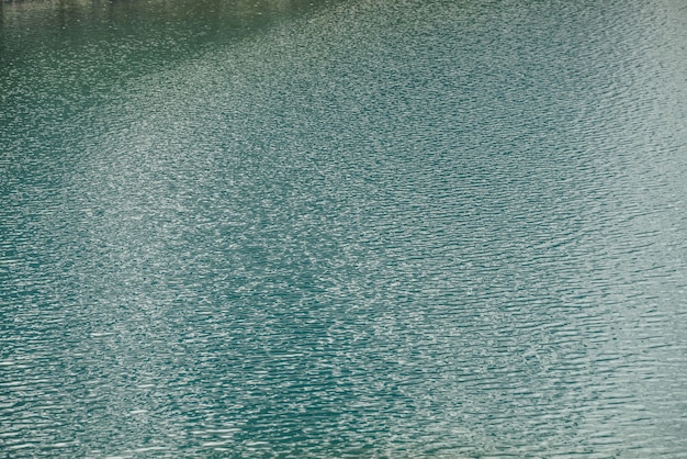 Фото Текстура зеленой голубой спокойной воды озера. медитативная рябь на поверхности воды. природа минимальный фон зеленого синего озера с золотым блеском. естественный фон фрагмента озера с чистой лазурной водой.