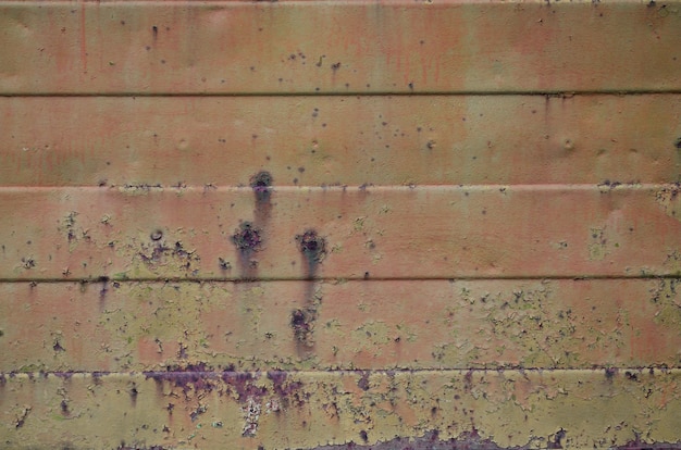 Texture of an old orange metal wall with significant damage from exposure to unfavorable weather conditions and dampness