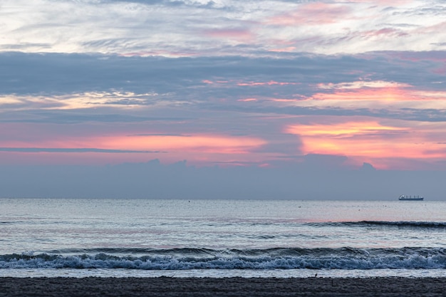 Текстурируйте морские волны на закате с розовыми облаками