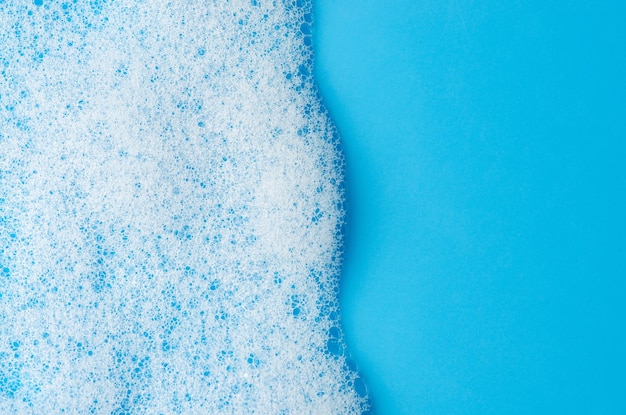 Texture of white foam on a blue background cleansing mousse for\
the face or bath foam or washing powder closeup copy space
