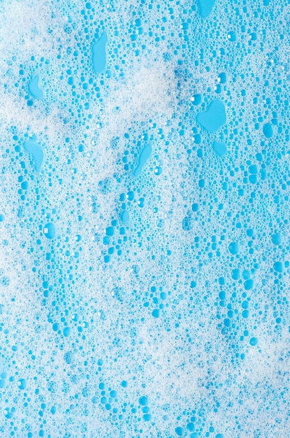 Photo texture of white foam on a blue background cleansing mousse for the face or bath foam or washing powder closeup