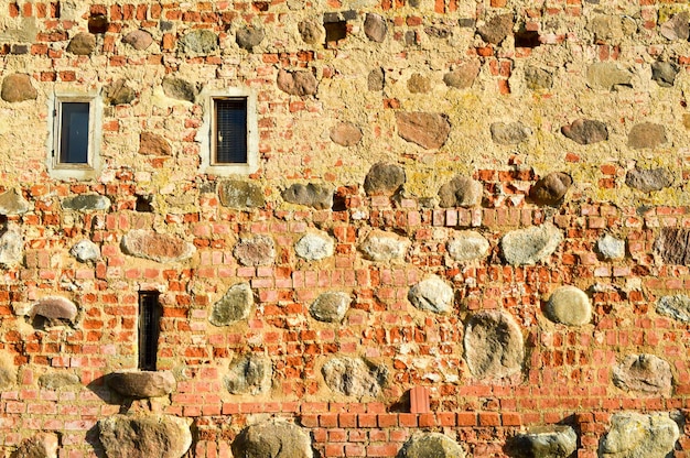 Texture with small narrow windows on an old ancient stone cracked dilapidated brick wall