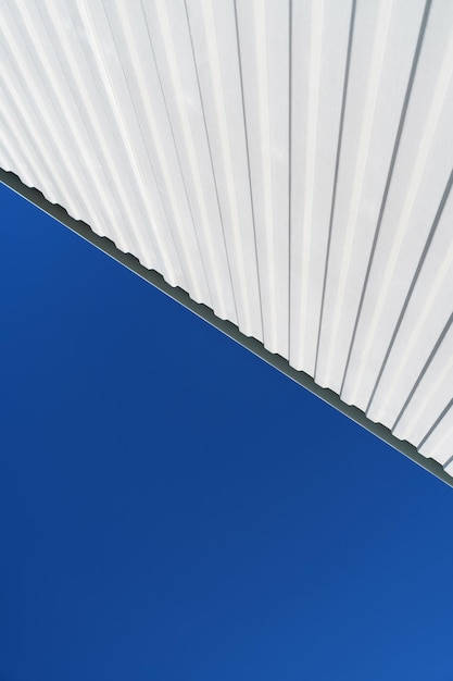 Textured white metal structures diagonally against a blue sky.