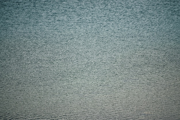 Textuur van donkerblauw kalm water van meer. Meditatieve rimpelingen op het wateroppervlak. Natuur minimale achtergrond van diepblauw meer. Natuurlijke achtergrond van helder donker turquoise water. Volledig kader van meerfragment.