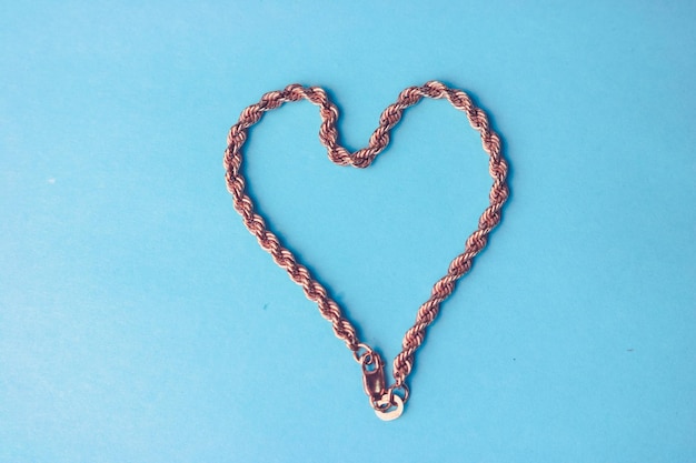 Foto textuur van een mooie gouden lieve feestelijke ketting van uniek weven in de vorm van een hart op een blauw