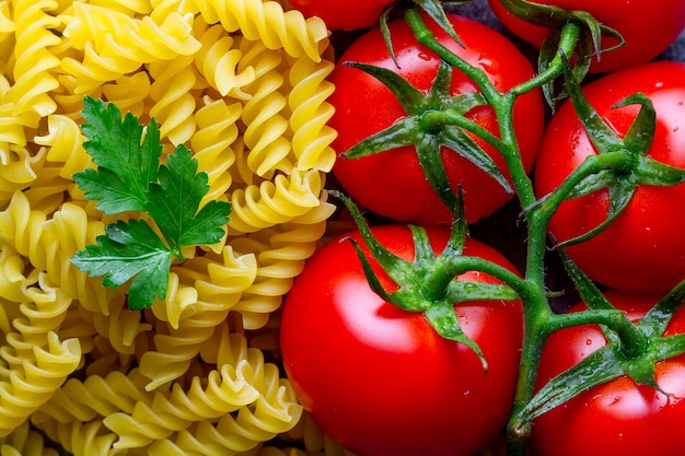 Textuur van ongekookte, gedroogde fusilli, verse tomaten en peterselie.