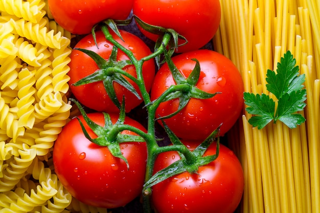 Textuur van ongekookte spaghetti, fusilli, peterselie en verse tomaten. Ingrediënten voor het koken van Italiaanse pasta