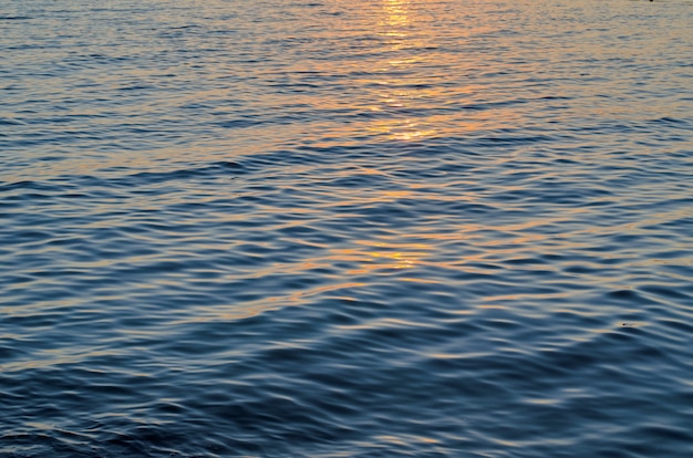 Textuur van zeewater bij zonsondergang, blauwe en oranje kleuren van zonweg