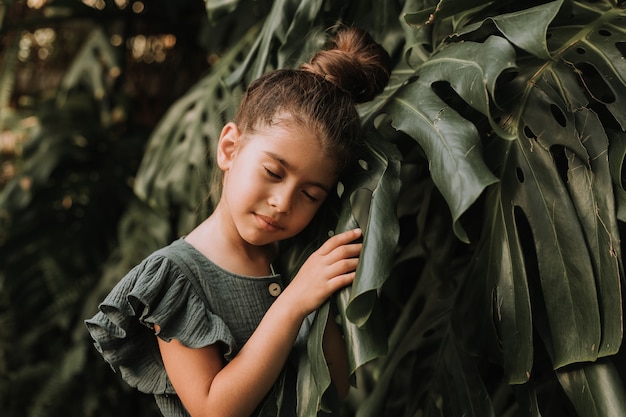 Tface of a little girl surrounded by tropical leaves Natural cosmetics cleanliness beauty concept