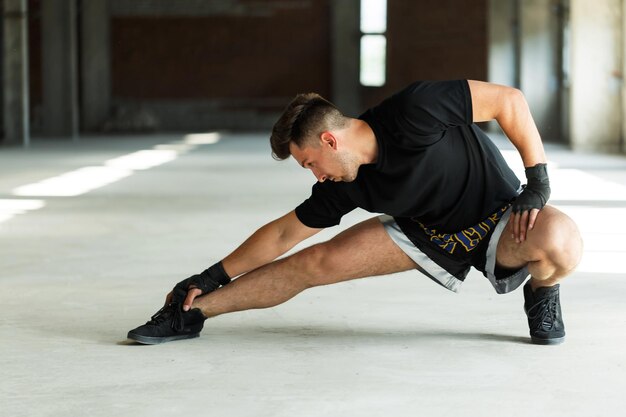 Thai boxer dressed in black tshirt and shorts fists with bandages warm up concept empty industrial place