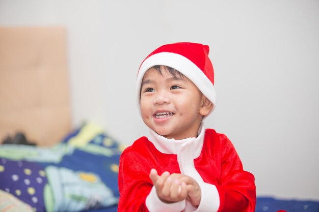 赤いサンタクロースの服を着たタイの男の子が幸せに笑顔でクリスマスを祝います