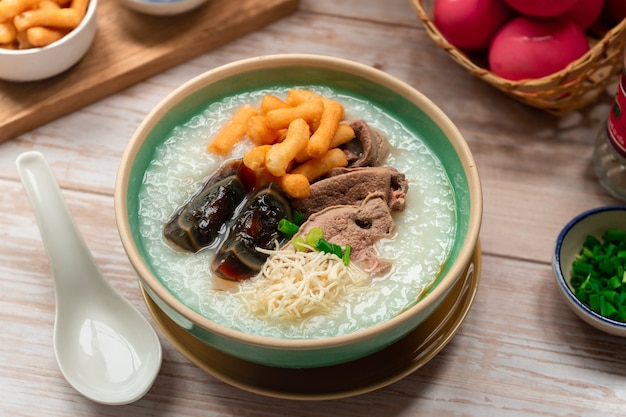 Thai breakfast Rice porridge with century egg and boiled river served on wooden surface