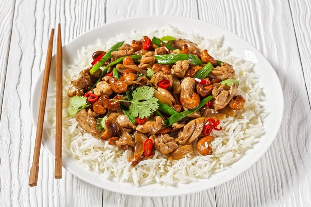 Thai cashew chicken stir fry served with a jasmine rice on a white plate on a wooden table with chopsticks horizontal view from above closeup