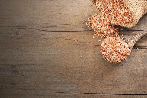 写真 タイの穀物食品木のスプーンと袋に入った赤い有機米玄米の上面図は、コピースペースのある木製のテーブルに横たわっていました