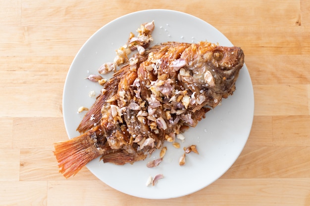 Thai deep fried fish with garlic served on white dish.