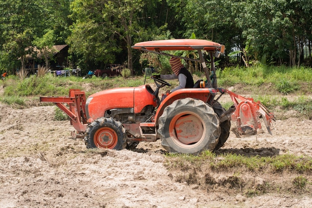 Thai farmers are using a tractor to prepare the soil for growing rice.