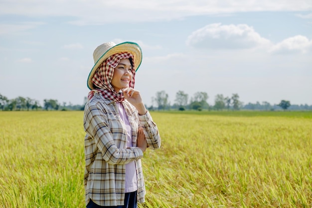 Thai female farmer in traditional dress and headdress standing smiling in the middle of the rice field