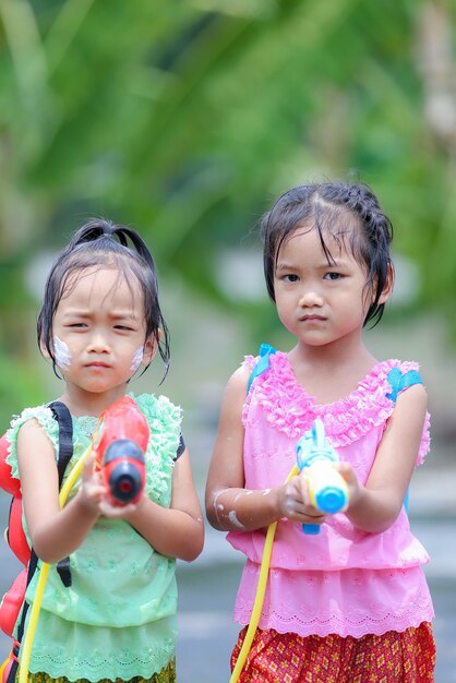 タイの時代のドレスとソンクラン祭りで水鉄砲を遊んでいるタイの女の子の子供たち