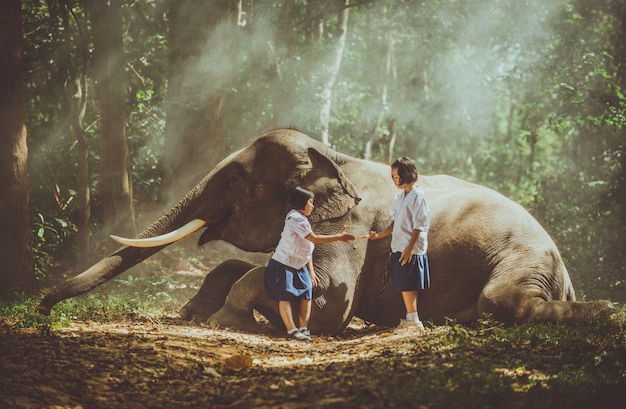 Thai  girls playing after school in the jungle near their elephant friend