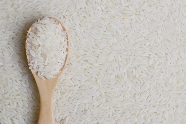 Photo thai jasmine rice in a wooden spoon on blurry jasmine rice background