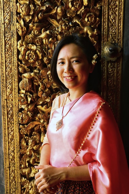 Thai lady in thai costume smiles and stand at thai wood carving art door