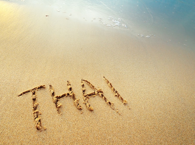 Foto lettere tailandesi scritte a mano in sabbia sulla spiaggia