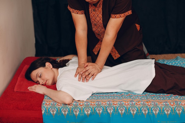 Thai man making classical thai massage procedure to young woman at beauty spa