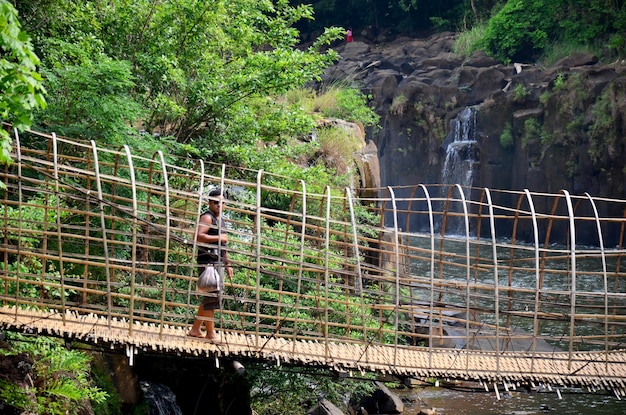 Thai man people travel and posing shooting photo on Suspension wooden and bamboo bridge for cross over stream river at Tad Pha Suam waterfalls in Pakse Champasak Laos