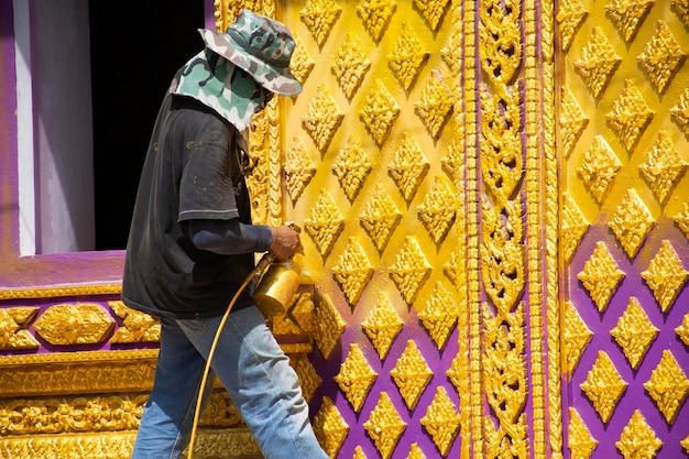 Thai man worker people and profesional builder working renovate build church and spray painting gold color ubosot or ordination halls of Wat Bang Chak temple at Pak Kret city in Nonthaburi Thailand