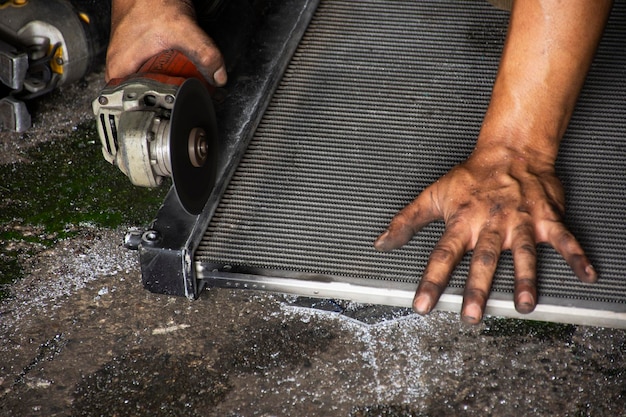 タイの男性技術者専門家は、タイのノンタブリーにある地元のガレージワークショップで、車のラジエーターのスチールカバーを切断する研削石の電気工作機械を使用して車両を修理します