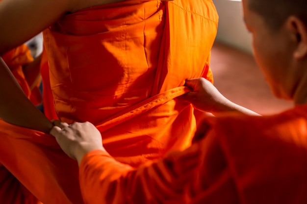 タイの僧kは、仏教徒が儀式で僧Monに状況を変えるためにオレンジ色の僧kの布を着るのを助けます。